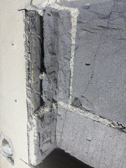 Hål i yttervägg med exponerat rör och skadad isolering, omgärdat av murverk. Vittnar om tidigare arbete, potentiellt kopplad till radiator.