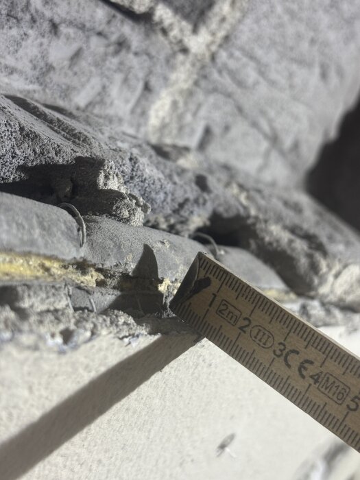 Mätband visar ett hål i ytterväggen med skadat isolerat rör synligt, över skev murad yta.