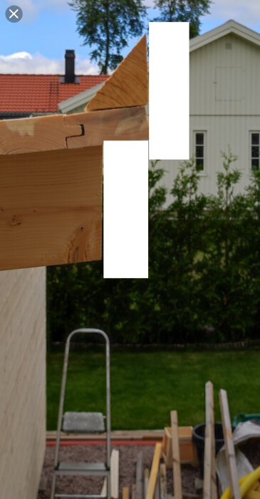 Vindskivor på takhörn monteras ovanpå ett tak med tegelhus och träd i bakgrunden. En stege och byggmaterial syns nedanför.