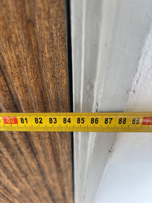 Måttband mäter avstånd vid dörrkarm i sommarstugan med eternitfasad.