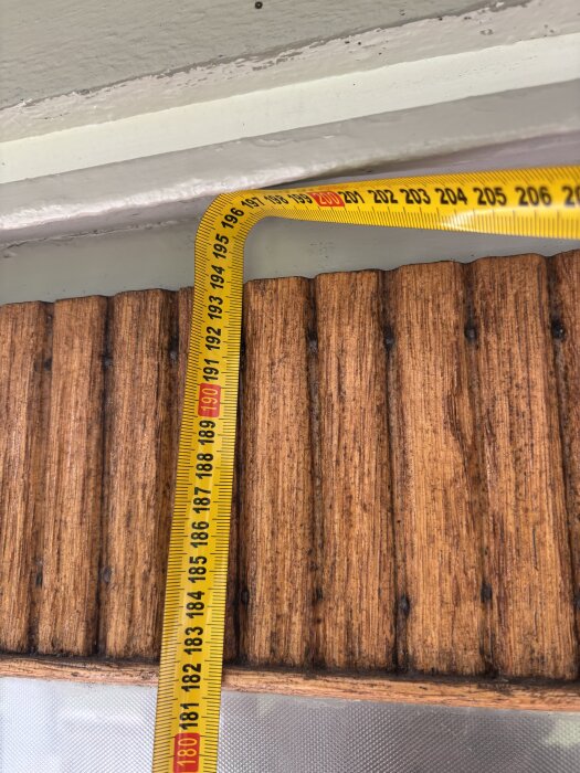Måttband ligger över vägg med brun eternitpanel, visar cirka 200 cm.