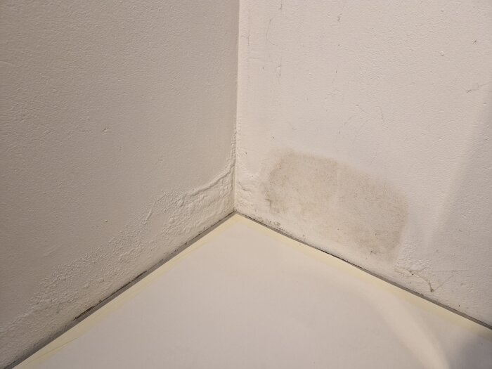 Fläckig vägg med bubblor i färgen och ett renare område där ett plastunderlägg har stått, indikering på renoveringsarbete.