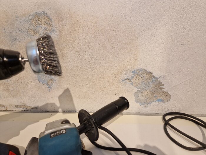 Stålborste och slipmaskin används för att avlägsna bubblor och gammal färg från en ojämn vägg.