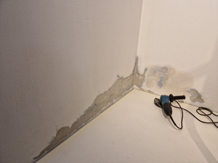 Vägg med bortskrapad färg och skador, slipmaskin på golvet.