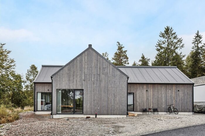 Modern träfasad av ett hus med gråtonad finish, omgiven av träd, med fokus på potential för järnvitriolbehandling.