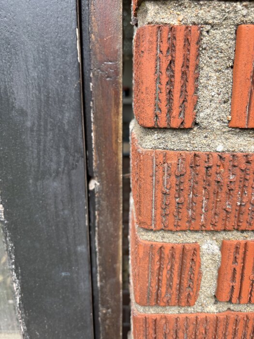 Närbild av träkarm och tegeldörröppning, med synlig spricka mellan karm och tegel.