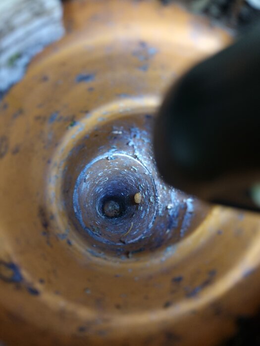 Vy ner i ett avloppsrör från en spolbrunn, delvis ockluderad av ett föremål längre ner i rörböjen, omgiven av rost och beläggningar.