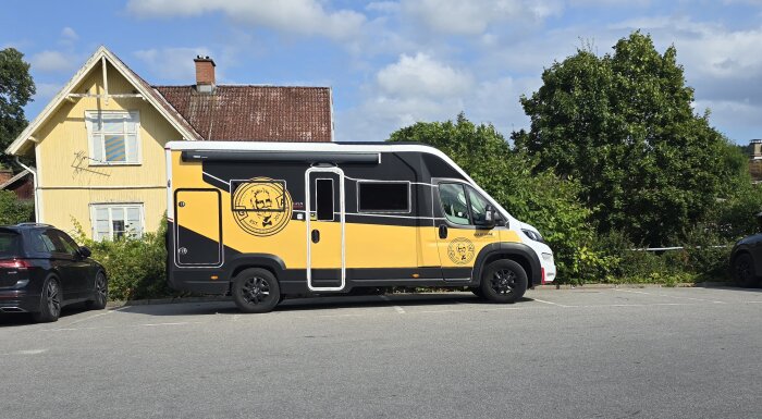 Gul och svart skåpbil parkerad framför ett gult hus, med logotyp på sidan av fordonet.