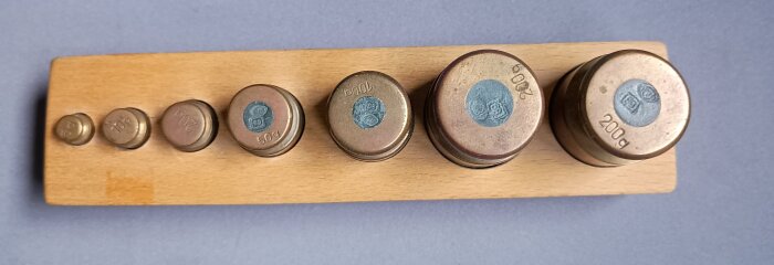 En uppsättning vikter i metall på en träbricka, märkta med olika gramvikter.