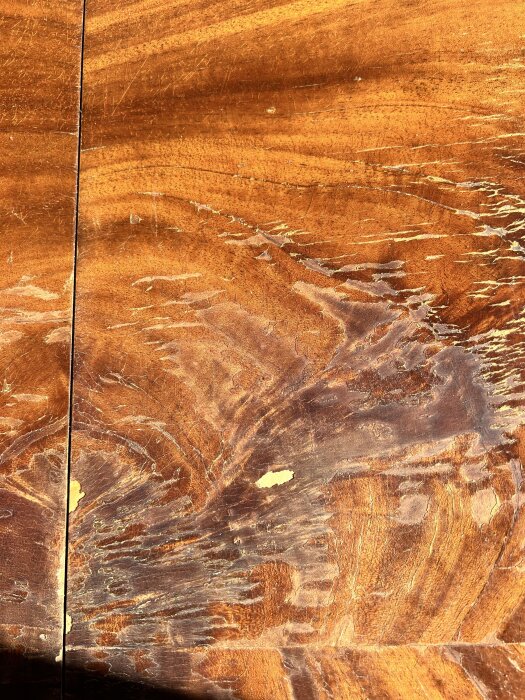 Gammalt träbord med krackelerad lackyta och små skador i faneret, potentiellt täckt av spröd shellack.