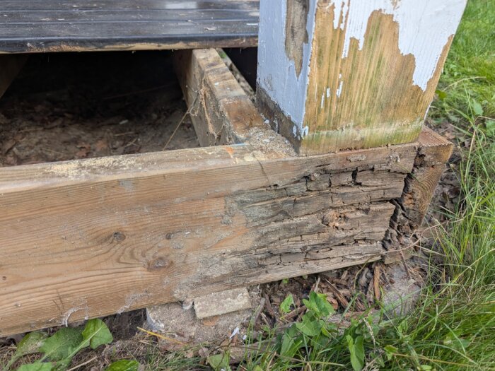 Ruttna träreglar och stolpe på balkong, målad med plastfärg, med vegetation runt omkring.