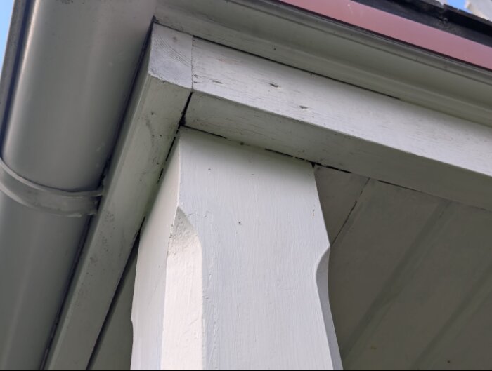 Vitmålad balkongstolpe och balkongregel med takränna ovanför, delvis i behov av renovering och målning med linoljefärg.