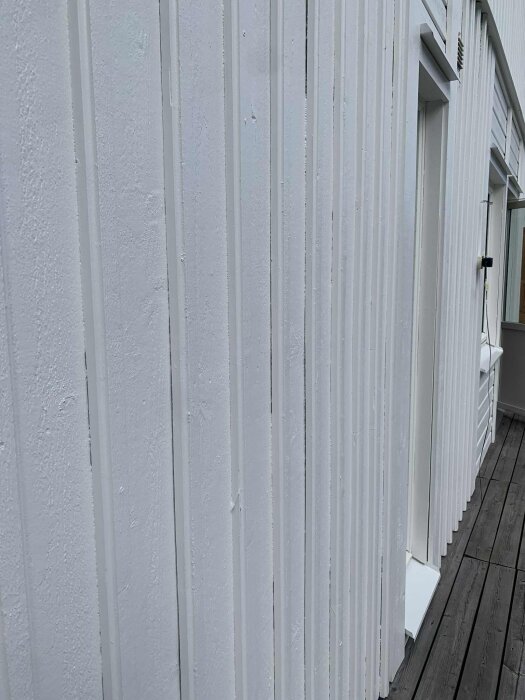 Vit lockläcktpanel med synliga glipor på en fasad, frågeställning om bästa sättet att åtgärda problemet med spikning eller fogning.