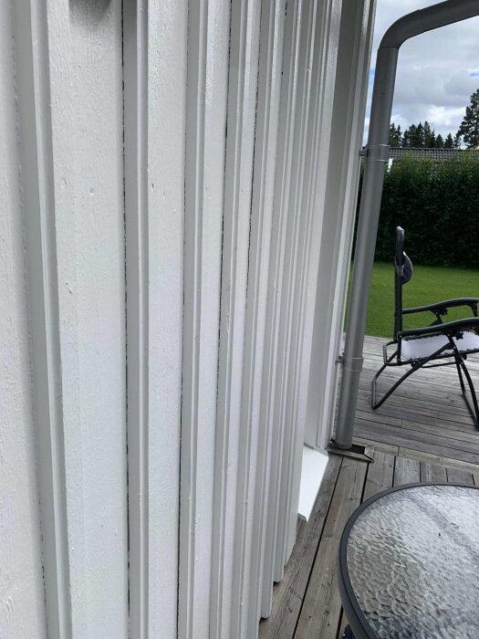 Vit lockläcktspanel med glipor på fasad, synlig altan med bord och stol i bakgrunden.