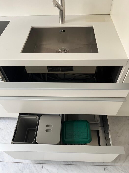 Varmvit köksbänk med undermonterad diskho, reglageblandare i metall, och utdragbar låda med sopkärl och insatser, del av Minotti-kök med Gaggenau.