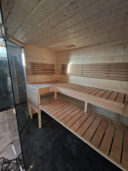 Nybyggd bastu med trälav och träpaneler, delvis återanvänd inredning. En modern bastu med glasdörr, sett från ingången.