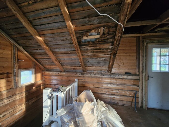 Ett tak med träpaneler och synlig skada, samt en trappa med verktyg och plastpåsar i ett renoveringsobjekt.