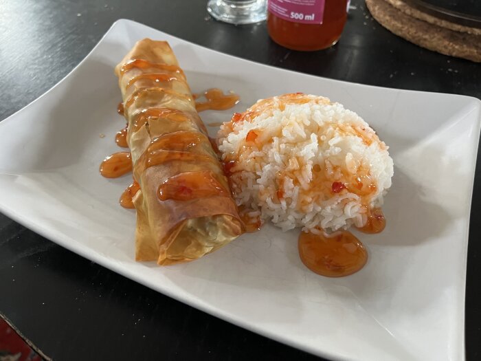 Hemmagjord vårrulle serverad med ris och sweetchilisås på en vit tallrik.