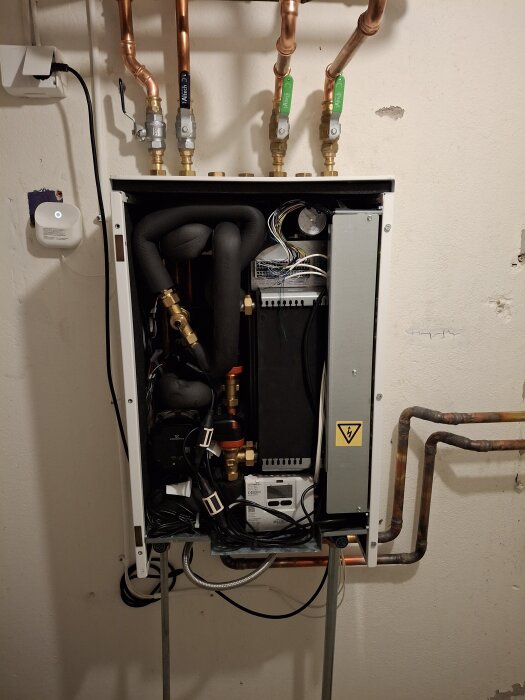 Fjärrvärmeväxlare installerad på en vägg med flera kopparrör, elkablar och ventiler.