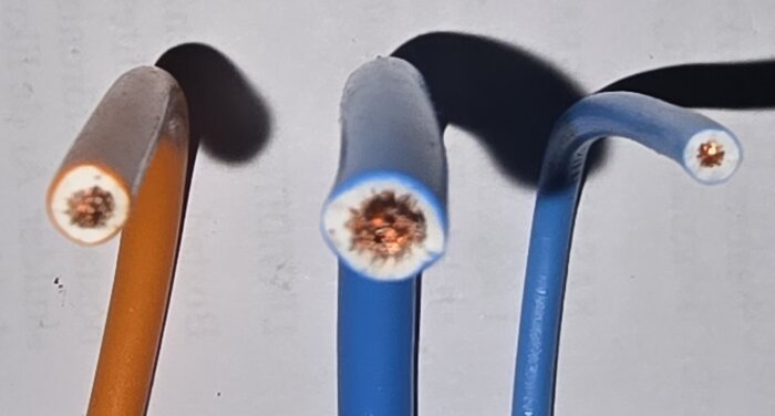 Tre böjda kablar i olika färger visas med tvärsnitt av ledarna synliga, en aspekt av isolering och ledningskapacitet.