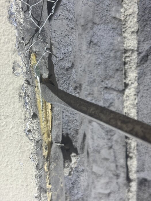 Närbild av ett grönt rör med skåra mot blottad metall, omgiven av isolering invirad i hönsnät, monterat på vägg.