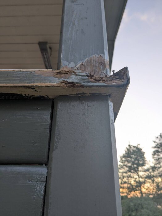 Trästolpe med synliga skador och flisor, monterad i en balkongkonstruktion. Stolpen visar tecken på både äldre färgrester och träförslitning.