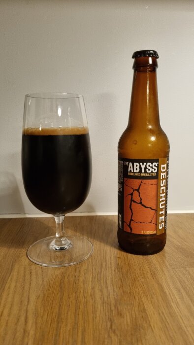 En flaska "The Abyss" stout och ett glas fyllt med mörk öl på ett träbord.