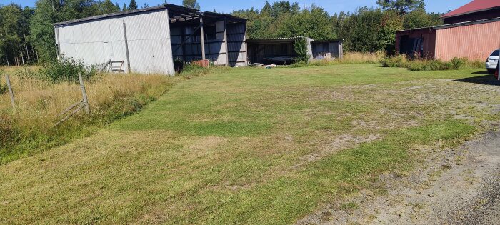 Nyklippt gräsmatta framför en äldre byggnad med omgivande natur och träd i bakgrunden.