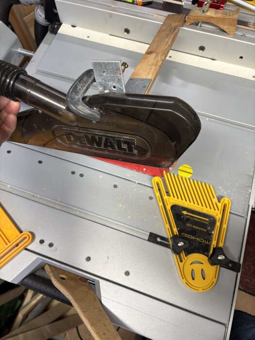 En Dewalt klinga med klingskydd monterat på en träribba med tving, mot t-spåret på ett sågverktyg, omgiven av trä och plastverktyg.