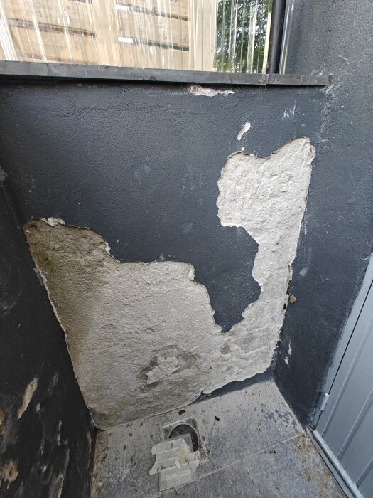 Skadad puts på källartrappa utomhus med sprickor och avflagningar. Resterande ytor färgade i mörk färg. Grått golv med smuts och skräp.