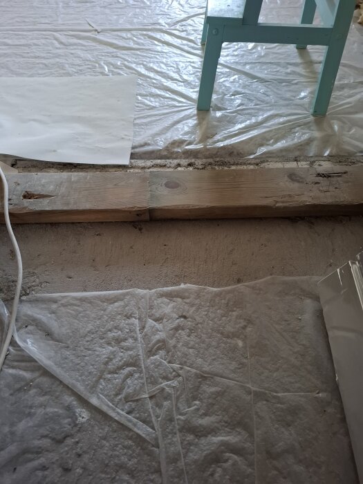 Dörröppning med bortkapad syll på betonggolv, plastskydd och trästol synlig i bakgrunden.