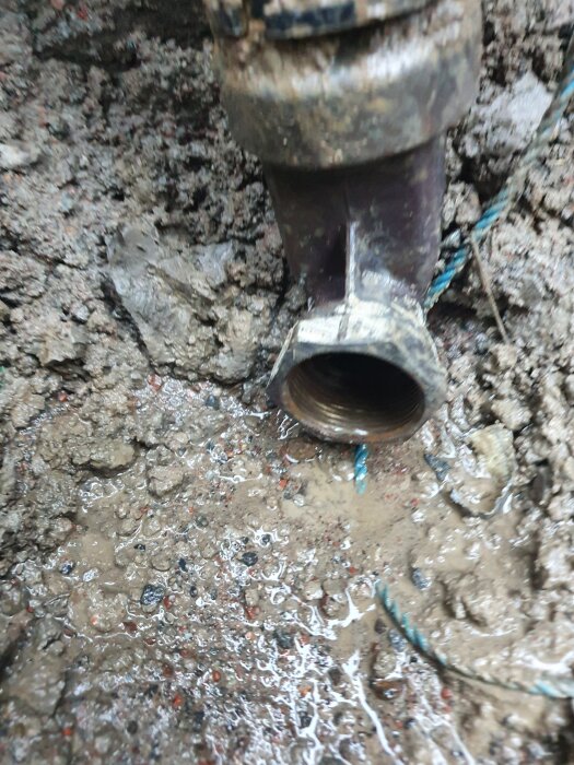 Bild på en kopplingsventil på servisledning inbäddad i lerig jord. Gängorna på ventilen är synliga, omgivet av våt och smutsig mark.
