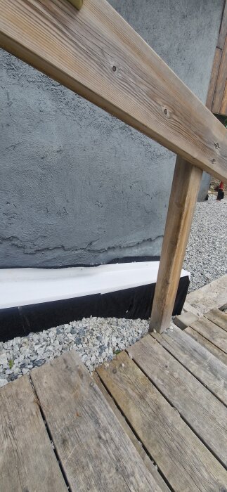 Trätrall med grus intill husvägg, listen och markduk synliga. Frågor om vattenskydd och isolering.