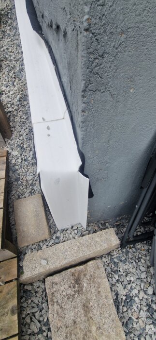 List och grus vid husgrund, med några stenar och träplankor runt, samt isoleringsmaterial som sticker ut ovan marknivå.