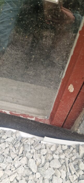 Fönster omgivet av röd list och grus, med ett streck av byggmaterial eller silikon ovanför gruset.