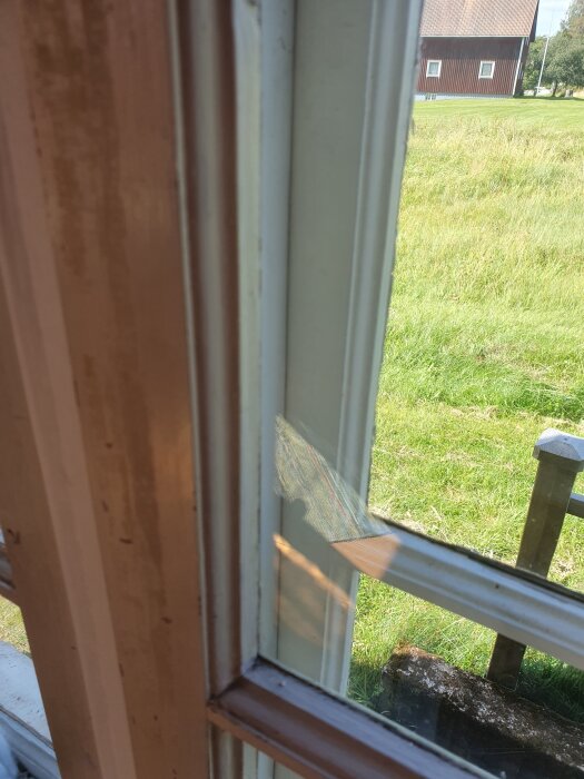 Närbild av originalfönster från 1923 med stor luftspalt; utsikt över gräsmatta och rött hus i bakgrunden.