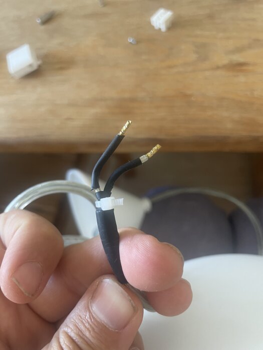 En hand håller två svarta kablar med guldiga klämmor i änden, förberedda för anslutning.