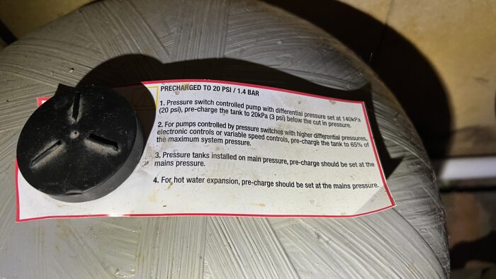 Etikett med instruktioner på en hydropress som beskriver förinställningar för trycktankens pre-charge vid olika tryckswitch-styrda situationer.