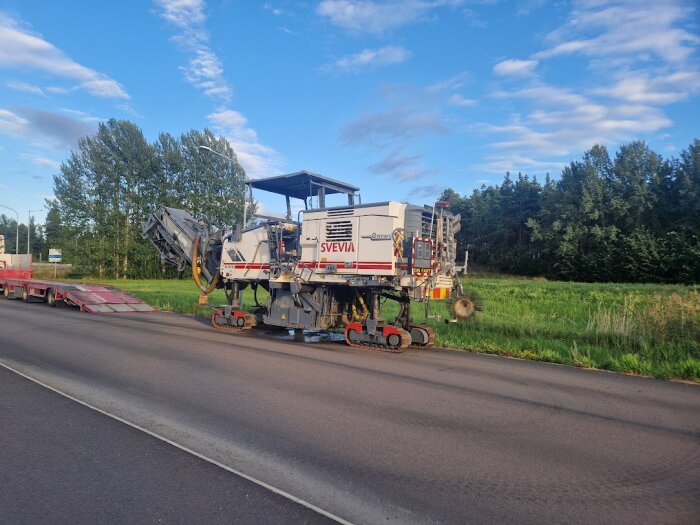 Festligt fordon med fyra små larvfötter på en landsväg; blå himmel och gröna träd i bakgrunden.