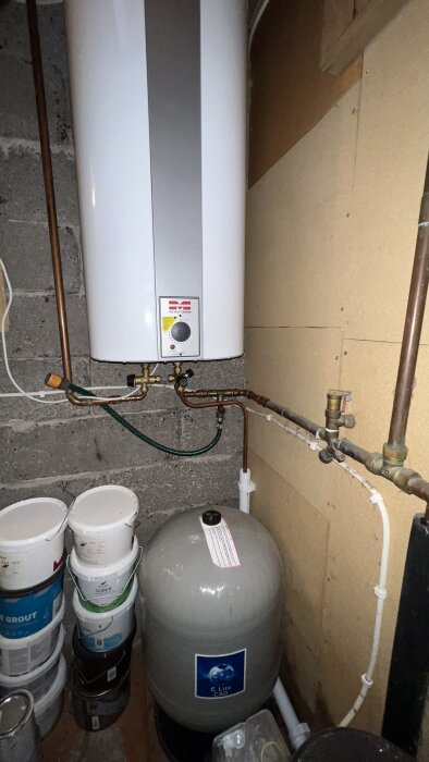 Vattenpump och trycktank i källare, omgiven av rör och färgburkar; diskussion om hydropress och tryckinställningar för gammal brunn.