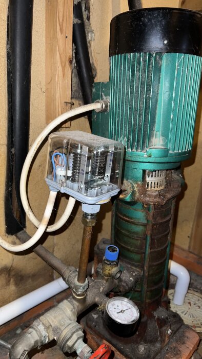 Äldre grön vattenpump med tryckströmbrytare och manometer i ett hus. Pumpen används för brunn med inställningsproblem.