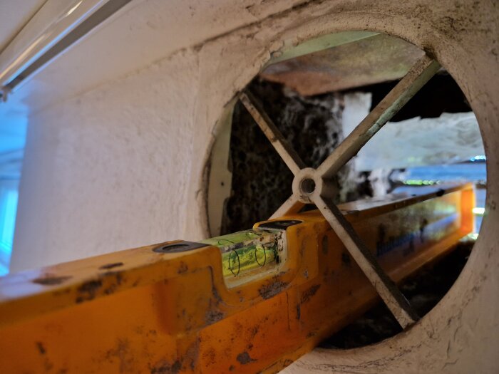 Nivå verktyg mot insidan av ett runt ventilationshål i en vägg, visar lutningen för rätt installation av ventilationsrör.
