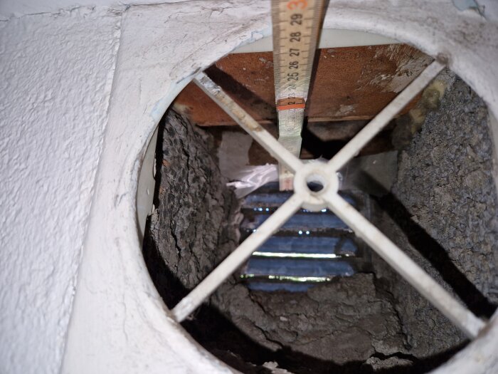 Ventilationsuttag med måttband, visar insidan av ett gammalt väggmonterat ventilationsrör med sprickor och det rektangulära hålets lutning.