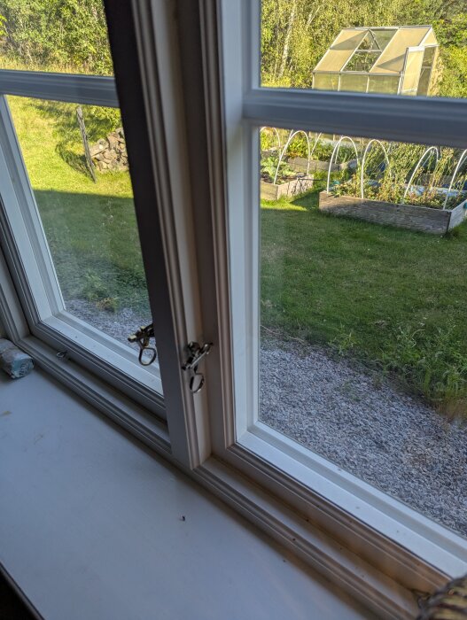 Gammaldags fönster med enkelglas och trädgård med växthus utanför, energiglas installerat i innerbågen för bättre isolering.