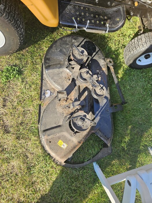 Klippaggregat på gräs intill en orange åkgräsklippare. Detaljer och slitage syns, en del ser trasig ut.