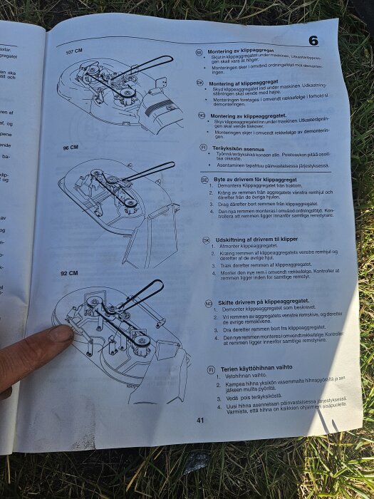 Användarmanual med sprängskisser och instruktioner för montering och byte av drivrem på ett klippaggregat, finger pekar på en del av diagrammet.