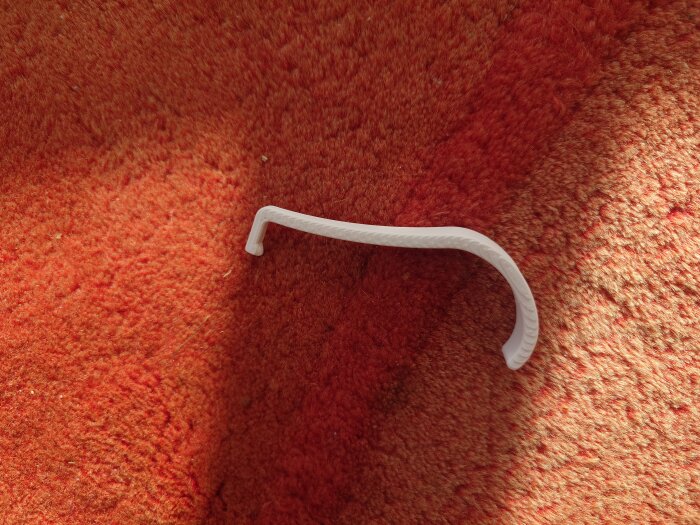 Vit, böjd plastklämma på röd matta, del av misslyckat klimattest där PLA inte tålde hög temperatur.