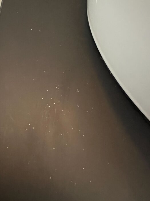 Svart bänkskiva med vita prickar nära ett handfat, orsakade av fukt.