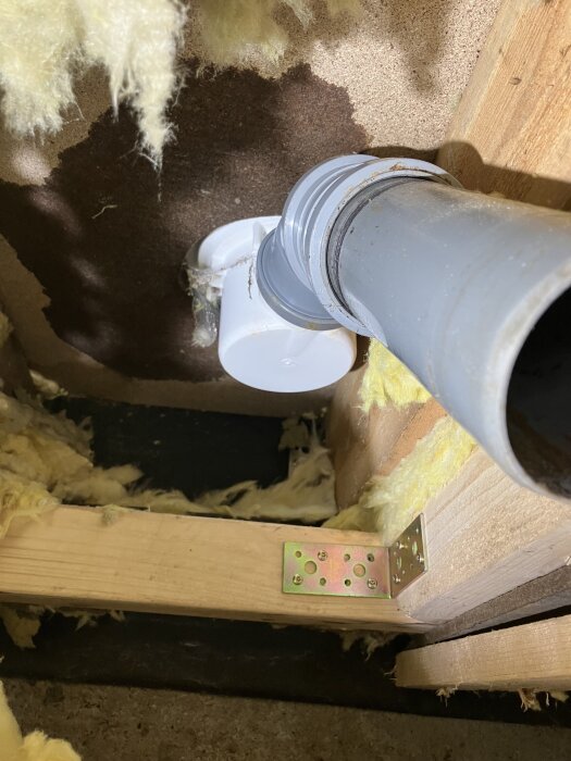 Rör och regelverk i trä med isolering i ett byggprojekt. Rören är inte korrekt placerade nära avloppet enligt texten.