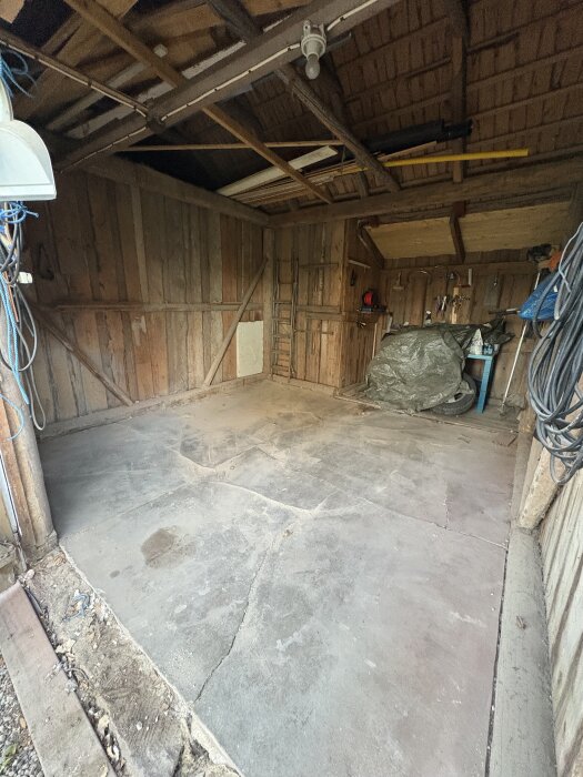 Gammalt uthus med sprucket betonggolv som planeras för renovering och isolering till snickarbod.